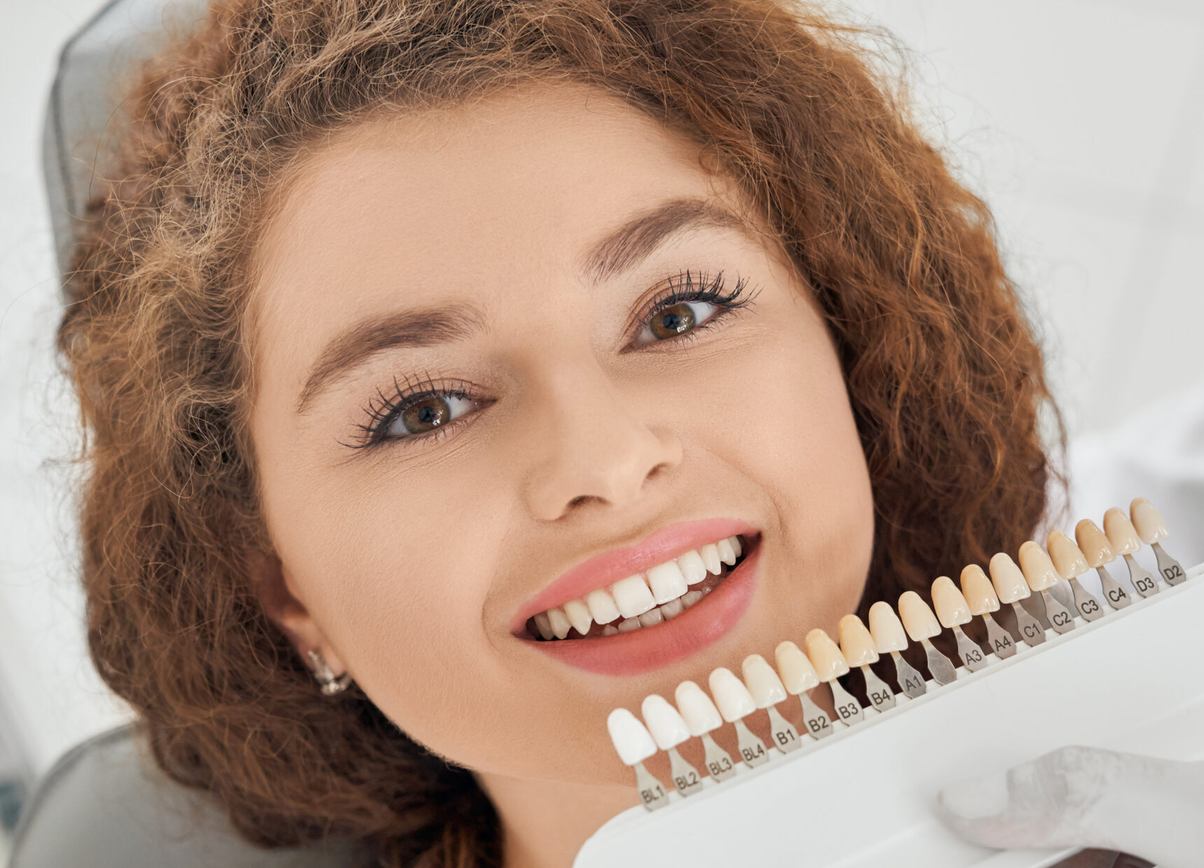 Woman smiling while male dentist keeping teeth color range